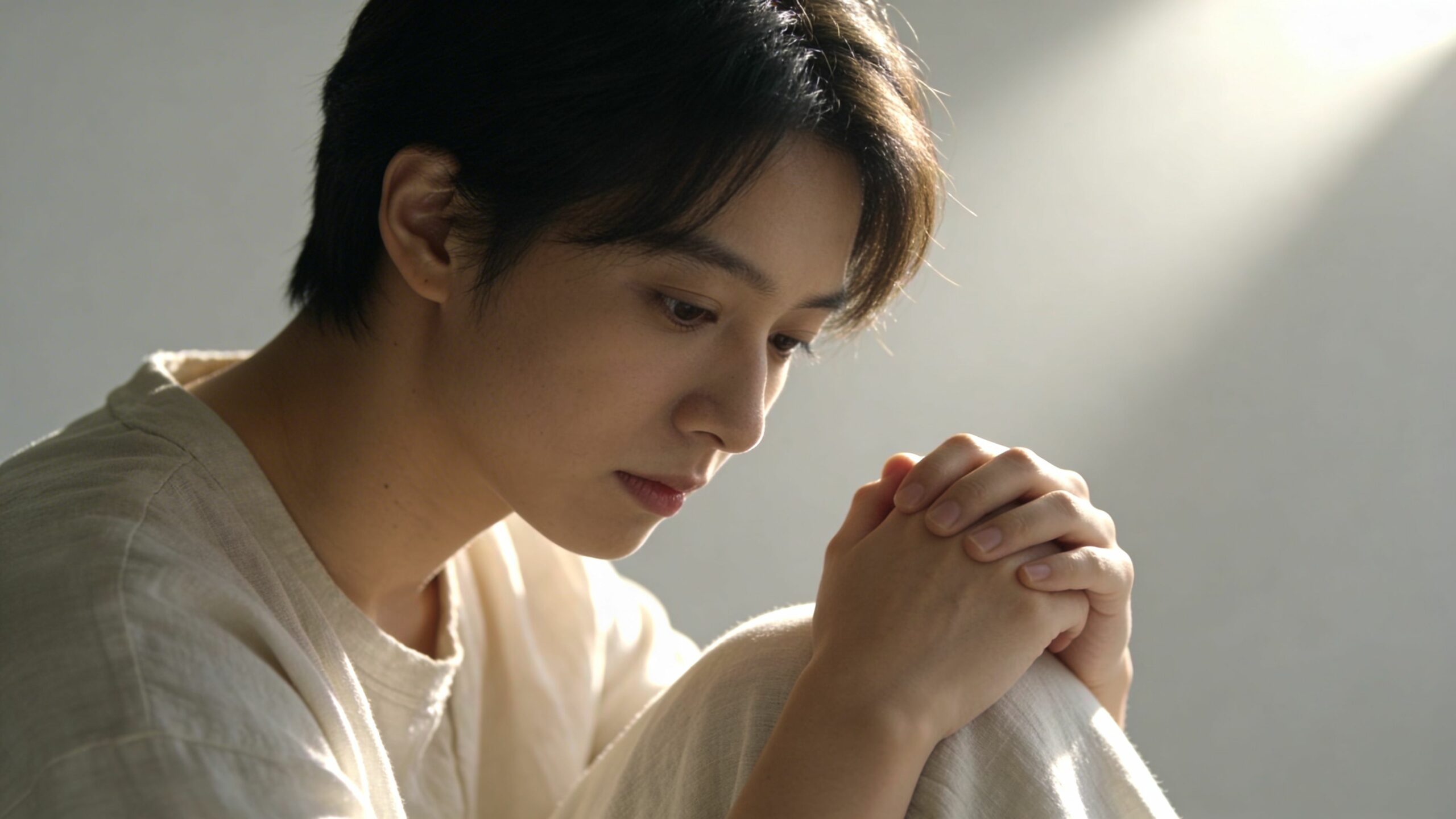 Jeune homme calme et pensif tenant ses mains jointes dans un moment de méditation ou de prière.