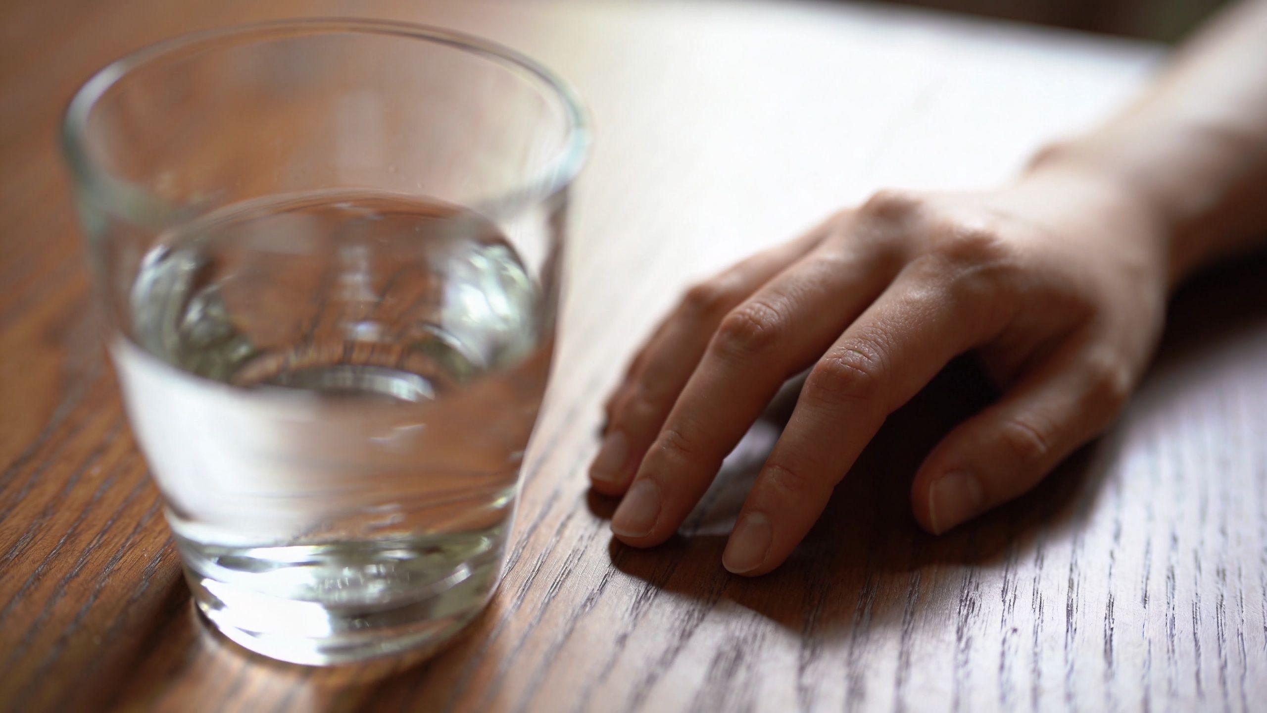 Une main posée sur une table en bois à côté d'un verre d'eau, symbolisant le soutien aux alcooliques.