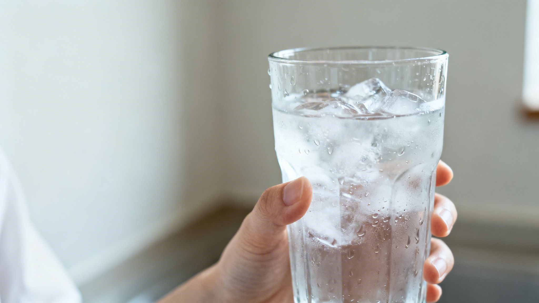 Main tenant un verre d'eau glacée rafraîchissante, avec des glaçons et de la condensation sur le verre.