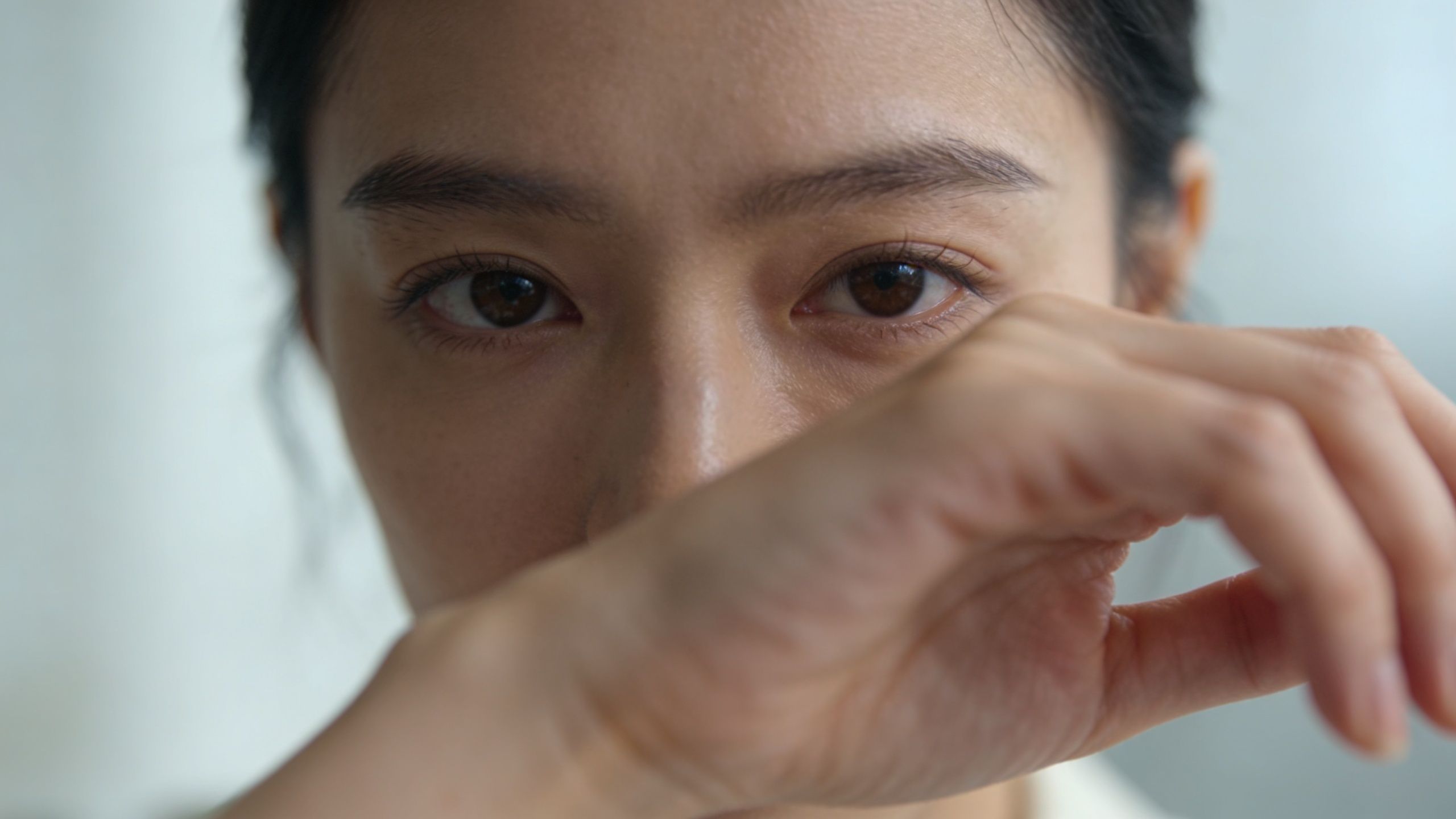 Gros plan sur le visage d'une jeune femme asiatique regardant la caméra avec une main devant elle.